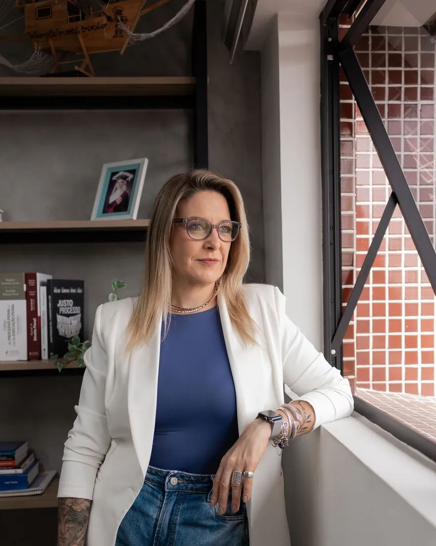 Renatta Höher junto à janela do escritório, ao lado da estante de livros